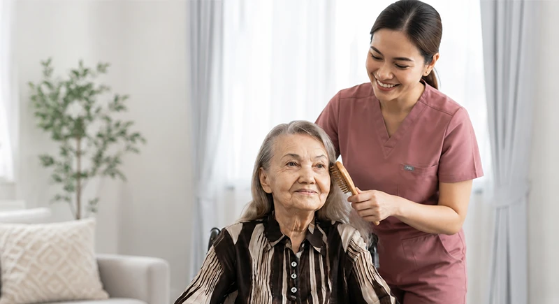 Caregiver providing personal care by brushing elderly woman's hair with a morning dress routine.