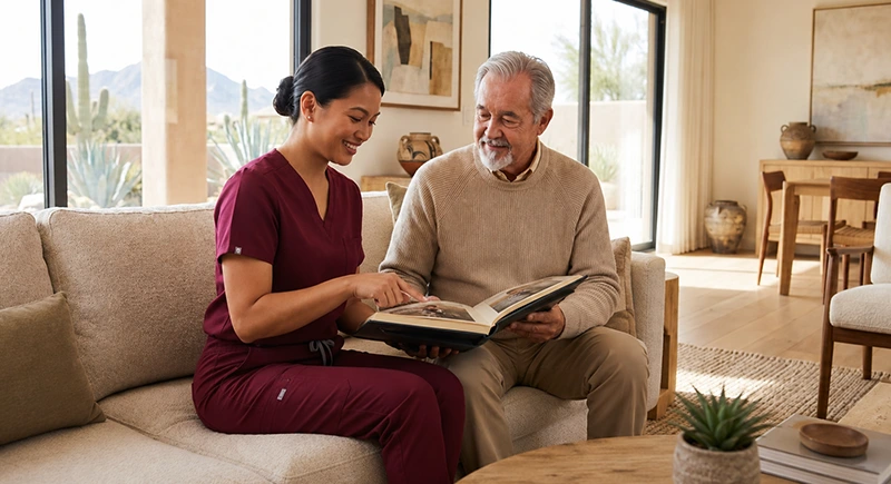 Caregiver is with elderly man with dementia on couch as they look at a photo album together.